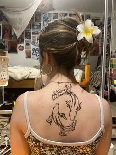 a woman with a tattoo on her back is looking at the mirror and she has a flower in her hair