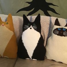 three knitted pillows with cats on them sitting on a couch next to each other