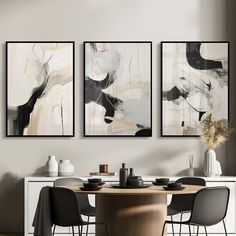 three paintings hang on the wall above a dining room table with black and white chairs