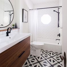 a white bathroom with black and white tile flooring, round mirror above the toilet