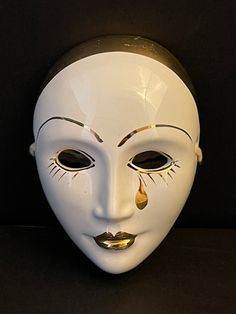 a white mask with gold details on the eyes and nose is shown against a black background