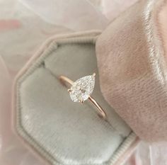 an engagement ring with a pear shaped diamond on it in a velvet box, close up