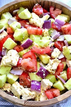 a salad with tomatoes, cucumbers, onions and feta cheese in a wooden bowl