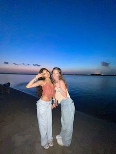 two women standing next to each other in front of the ocean at night with their arms around each other