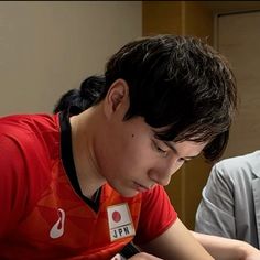 a young man sitting at a table writing on a piece of paper