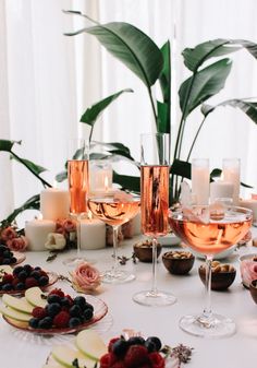 a table topped with plates and glasses filled with fruit next to candlelight votives