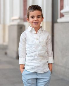 a young boy standing on the sidewalk in front of a building wearing blue pants and a white shirt