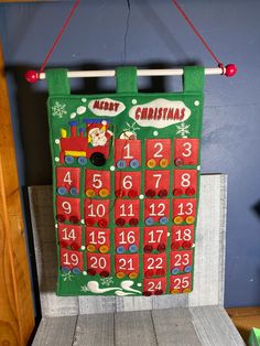 a green christmas calendar hanging from a wooden frame on a wall in front of a blue wall