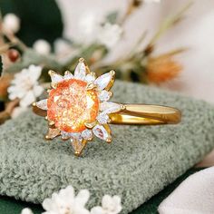 an orange diamond ring sitting on top of a green cloth next to white and pink flowers