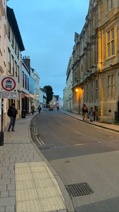 people are walking down the street in front of some buildings at dusk, and one person is on his cell phone