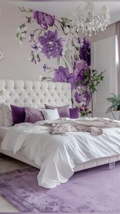 a bedroom decorated in purple and white with flowers on the wall above the bed, along with chandelier