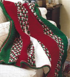 a crocheted afghan is draped on a couch with a blanket that has red, green and white stripes