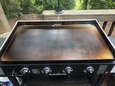 an outdoor grill with two burners on the top and one is black stone, in front of a wooded area