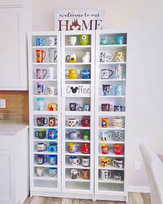 two glass shelves with coffee mugs on them in a white kitchen, next to a dining room table