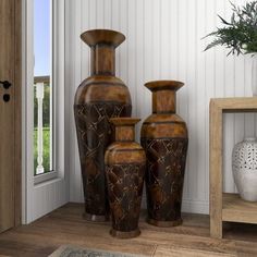 three brown vases sitting next to each other on a wooden floor in front of a window