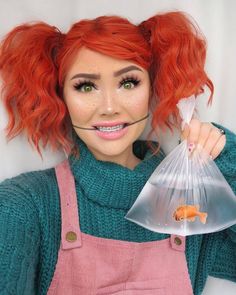 a woman with red hair and green eyes holding a plastic bag filled with fish in it