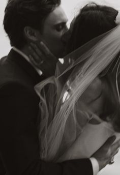 a bride and groom kissing each other in front of the camera with veil over their heads