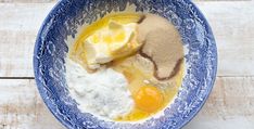 a blue bowl filled with eggs, flour and other ingredients on top of a wooden table