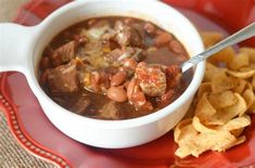 a red plate topped with a bowl of chili and tortilla chips