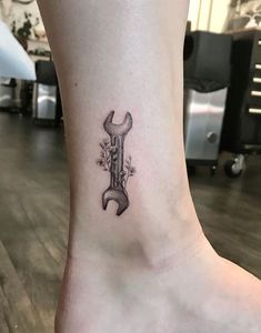 a small tattoo on the foot of a person with a wrench and flowers in it