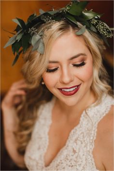 a woman wearing a flower crown with leaves on her head and eyes closed, smiling at the camera