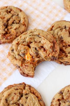 several chocolate chip cookies are on a white tablecloth and one cookie is broken in half