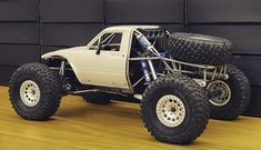 a white truck with four wheels and big tires parked in front of a black wall