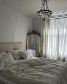 an unmade bed with white sheets and pillows in front of a large chandelier