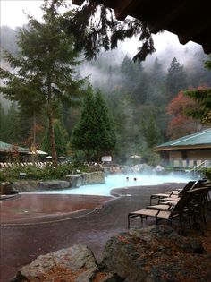 an outdoor swimming pool surrounded by trees and fog in the distance, with several lounge chairs around it