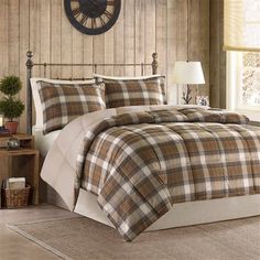 a bed with plaid comforter and pillows in a bedroom next to a clock on the wall