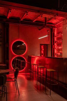 a dimly lit restaurant with red lighting and round mirrors on the wall, along with bar stools