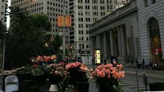 flowers are sitting on tables in the middle of a city street with tall buildings behind them