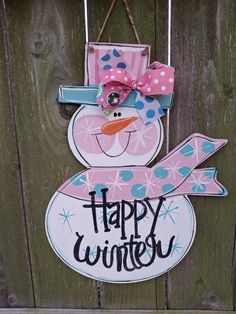 a sign that says happy winter hanging from a wooden fence with a snowman on it