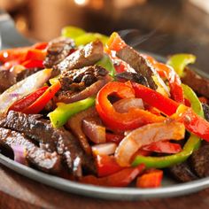 a plate full of beef and peppers on a wooden table