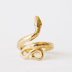 In front of a white background is a gold snake ring. The tail is at the bottom and the body and head curves around to the top of the ring. Adjustable Symbolic Snake-shaped Jewelry, Spiritual Brass Snake-shaped Jewelry, Spiritual Brass Jewelry In Snake Shape, Adjustable Snake Symbolic Ring, Adjustable Symbolic Snake Ring, Adjustable Snake-shaped Symbolic Rings, Symbolic Adjustable Snake Ring Gift, Adjustable Symbolic Snake Ring Gift, Symbolic Snake-shaped Brass Jewelry