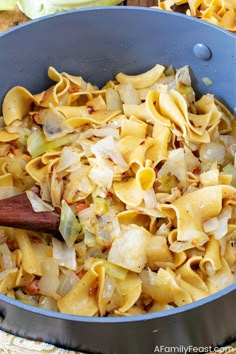 a pan filled with pasta and vegetables on top of a table next to a wooden spoon