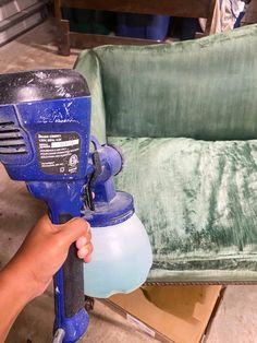 a person is holding a blue sprayer in their hand and it's next to a green couch