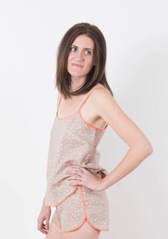 a woman standing in front of a white wall wearing a tan tank top and pink panties