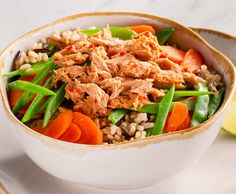 a white bowl filled with meat and veggies next to a slice of lemon