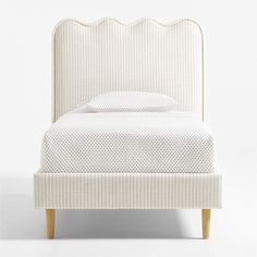 an upholstered bed with white linens and wooden legs, against a white background