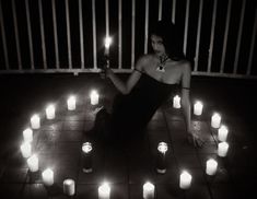 a woman sitting on the ground surrounded by candles with one candle lit in front of her