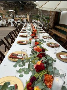 a long table is set with place settings and flowers on it for an outdoor dinner