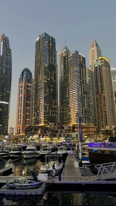 boats are docked in the water next to some tall buildings and skyscrapers at night