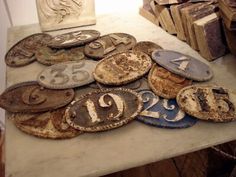 an assortment of old and rusty metal numbers on a table with stacks of books in the background