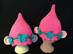 two crocheted hats with flowers on them sitting next to each other in front of a black background