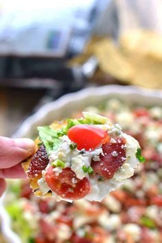 a hand holding a piece of food with tomatoes and lettuce on it in a bowl