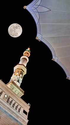 an illuminated clock tower with the moon in the sky above it and a blue canopy over it