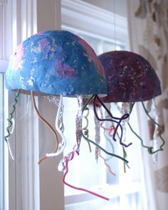 two jellyfish like objects hanging from the ceiling in front of a window with curtains