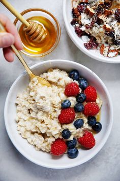 two bowls filled with oatmeal, berries and honey