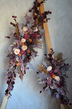 two tall wooden poles with flowers and foliage hanging from the wall next to each other